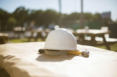 White construction hard hat and hammer on a picnic table outside in sunny Pensacola, FL setting.